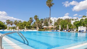 A swimming pool with lounge chairs and umbrellas, surrounded by palm trees and buildings. - Yadis Hammamet Club (Hammamet)
