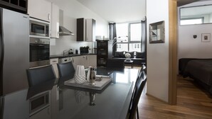 A modern kitchen with stainless steel appliances, a dining area with a glass table, and a view of a cityscape through large windows. - Máni Apartments by Heimaleiga (Reykjavik)