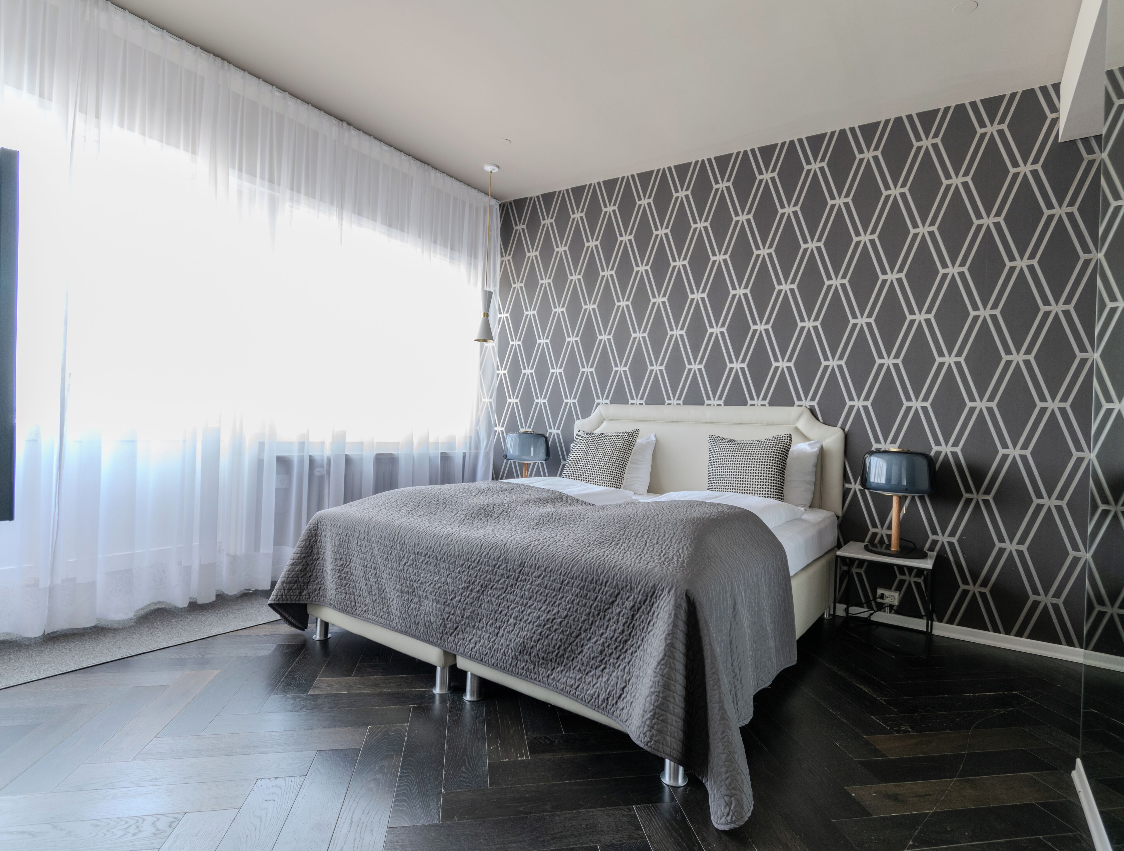 A modern bedroom with a large bed, a bedside lamp, and a geometric patterned wall.
