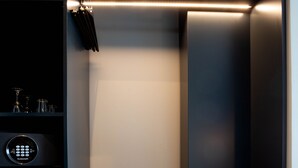 A modern, dark-colored walk-in closet with a built-in bench, a control panel, and a shelf with glassware. - Máni Apartments by Heimaleiga (Reykjavik)