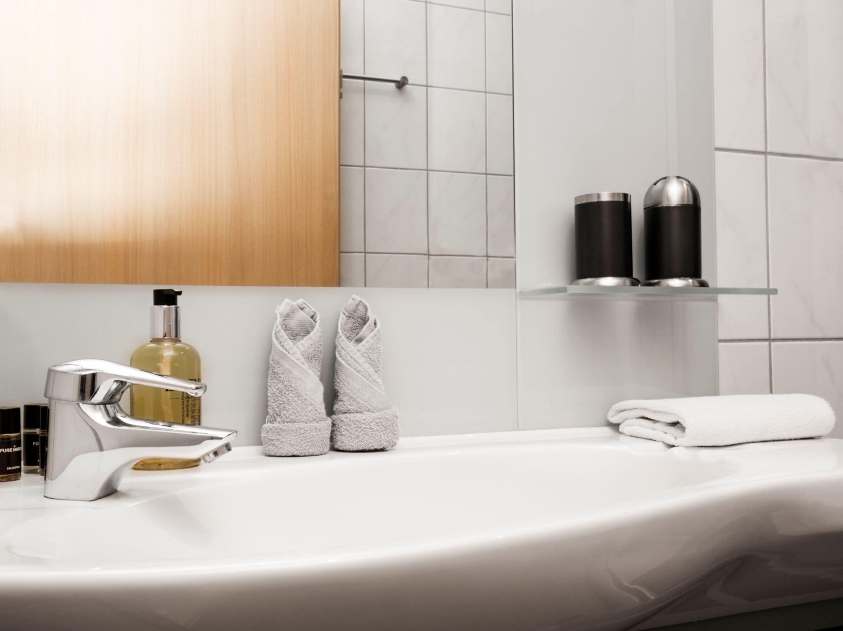 A bathroom with a white sink, chrome faucet, and two bottles on a shelf.