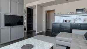 A modern living room with a flat-screen TV, a sofa, a coffee table, and a kitchen area with a microwave and cabinets. - Máni Apartments by Heimaleiga (Reykjavik)