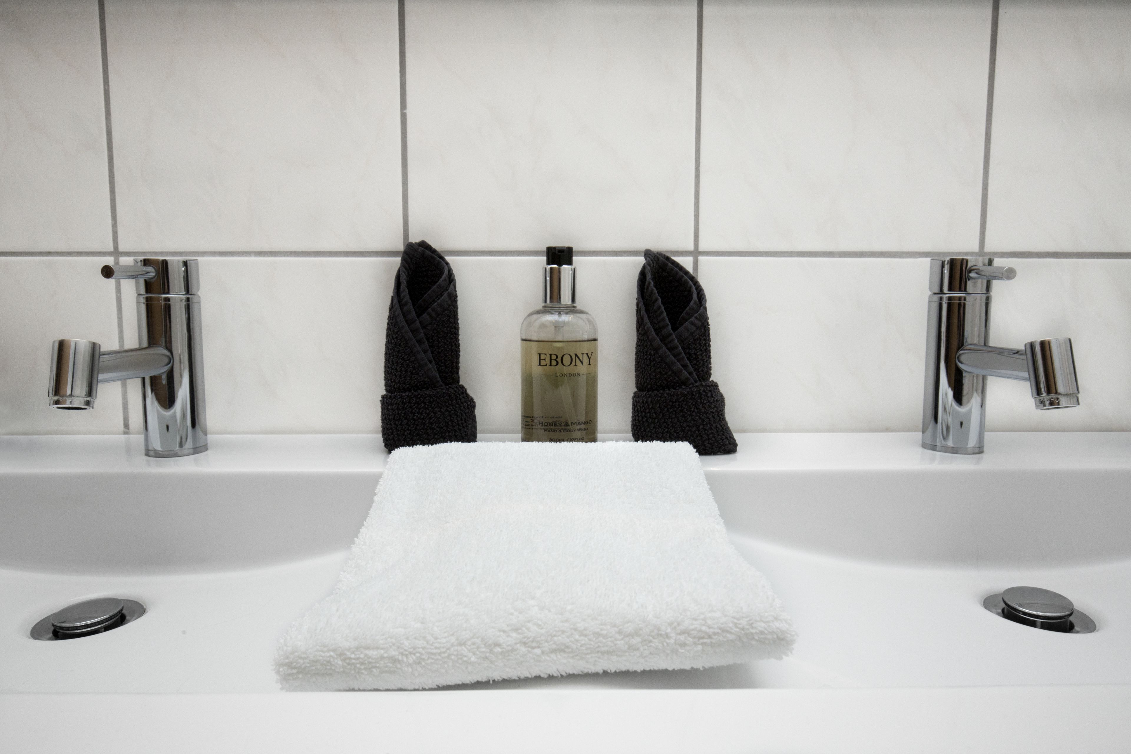Un baño con un lavamanos blanco, dos llaves, una botella de jabón líquido y dos toallas.