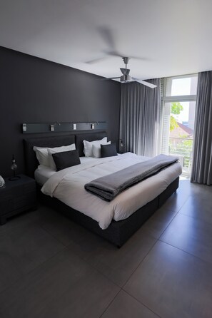 A modern bedroom with a large bed, a ceiling fan, and a view of the outdoors through a large window. - Atlantic Affair Boutique Hotel (Cape Town)