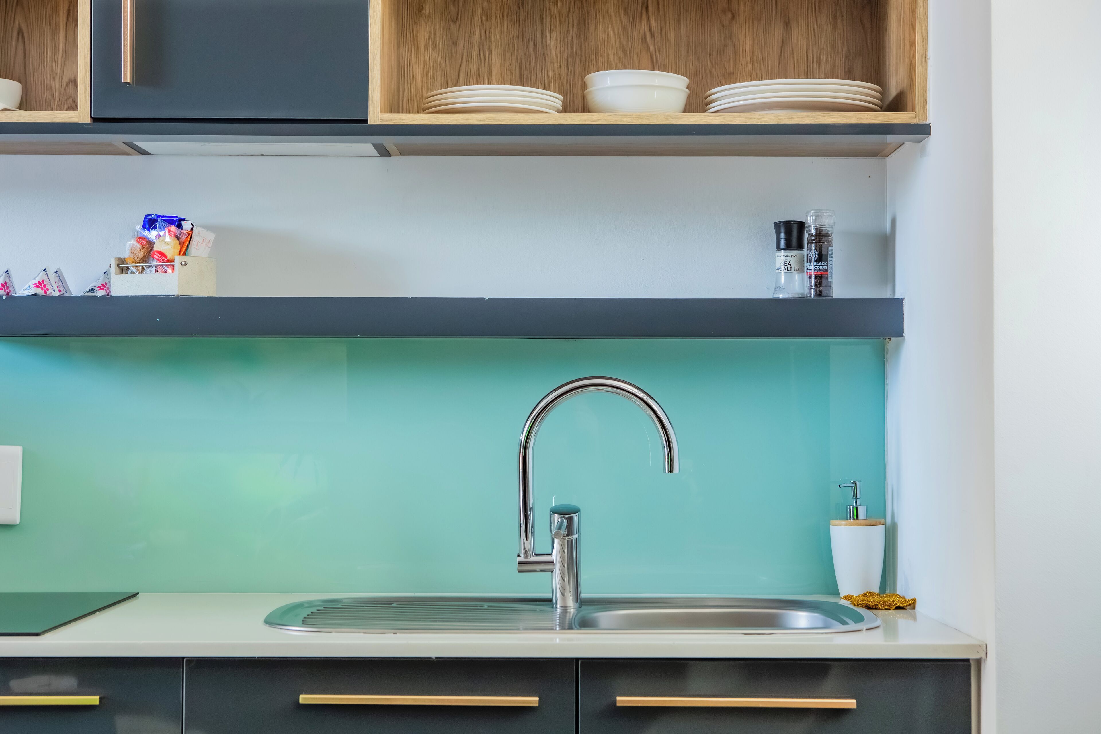 Eine moderne Küche mit türkis-blauer Spritzschutzwand, einer Edelstahl-Spüle und Holzschränken.