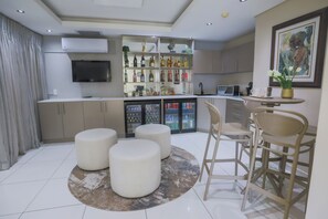 A modern kitchen with a built-in wine rack, a refrigerator, and a dining area with stools and a table. - Atlantic Affair Boutique Hotel (Cape Town)