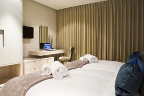 Ein Hotelzimmer mit einem Bett, einem Schreibtisch mit einem Laptop, einem Fernseher und einem großen Fenster mit Vorhängen.