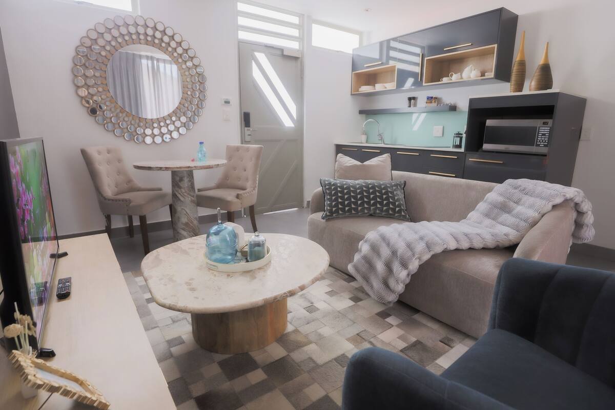 Un salon moderne avec une table basse ronde, un canapé agrémenté d’un plaid et un coin repas composé de deux chaises et d’une petite table.