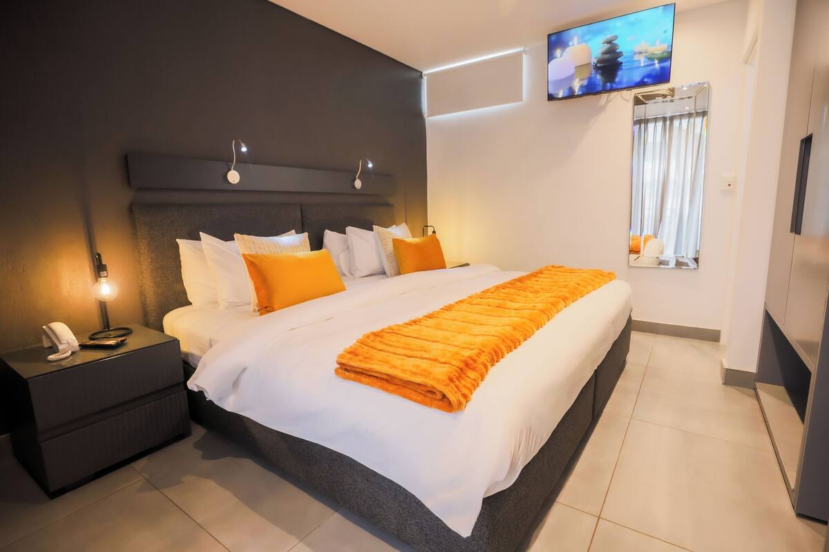 Une chambre d’hôtel moderne avec un grand lit, une table de chevet avec un téléphone, un téléviseur fixé au mur et un miroir.