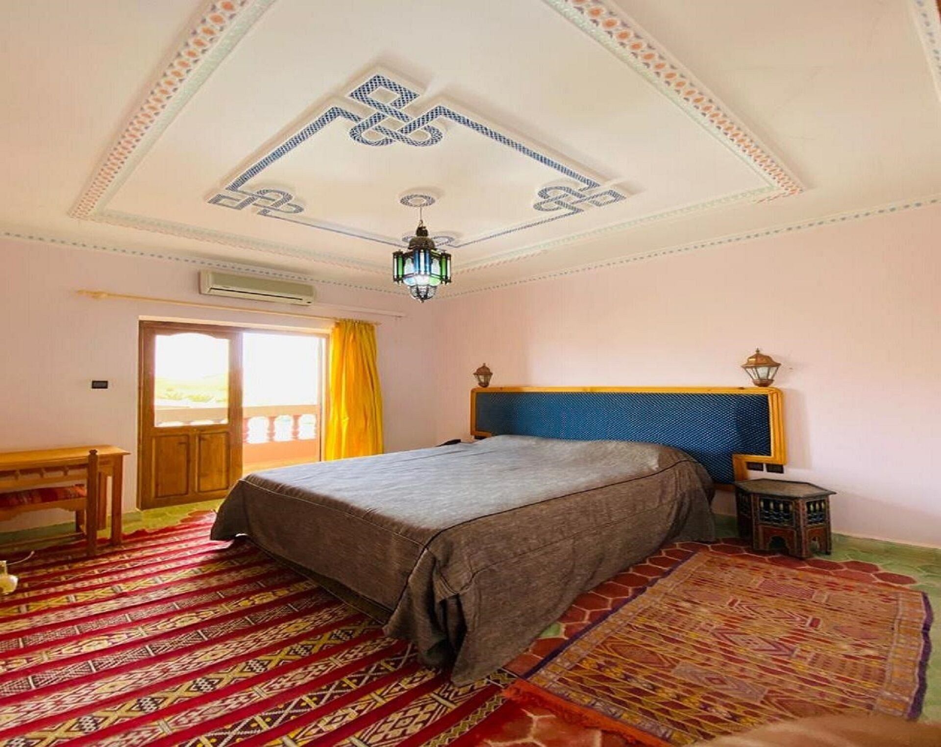 Une chambre à coucher comprenant un lit, une table de chevet, une lampe, un ventilateur de plafond et un tapis à motifs.