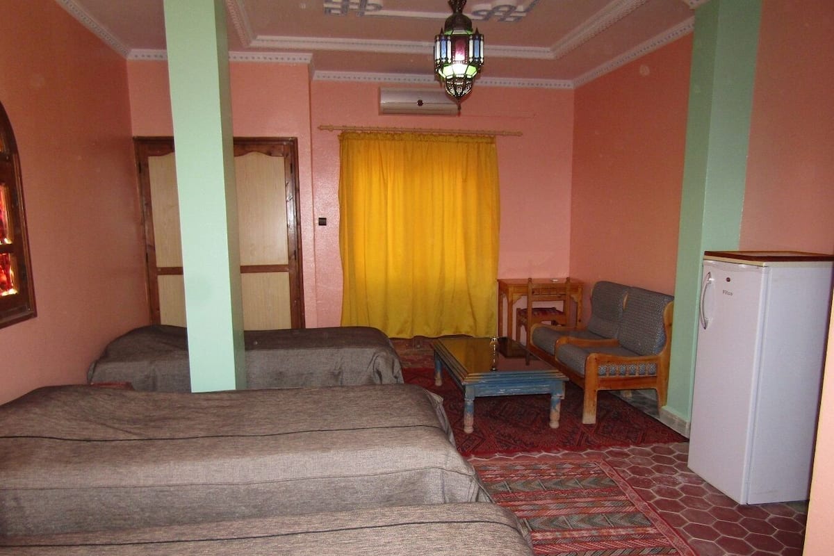 Une chambre avec deux lits, une petite table, un canapé, un réfrigérateur et un tapis à motifs.