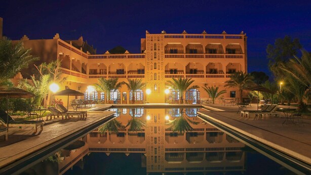 Ein Hotel mit großem Pool, Palmen und dem Gebäude-Spiegelbild im Wasser.