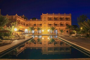 A hotel with a large pool, palm trees, and a reflection of the building in the water. - La Perle du Draa Hotel (Zagora)