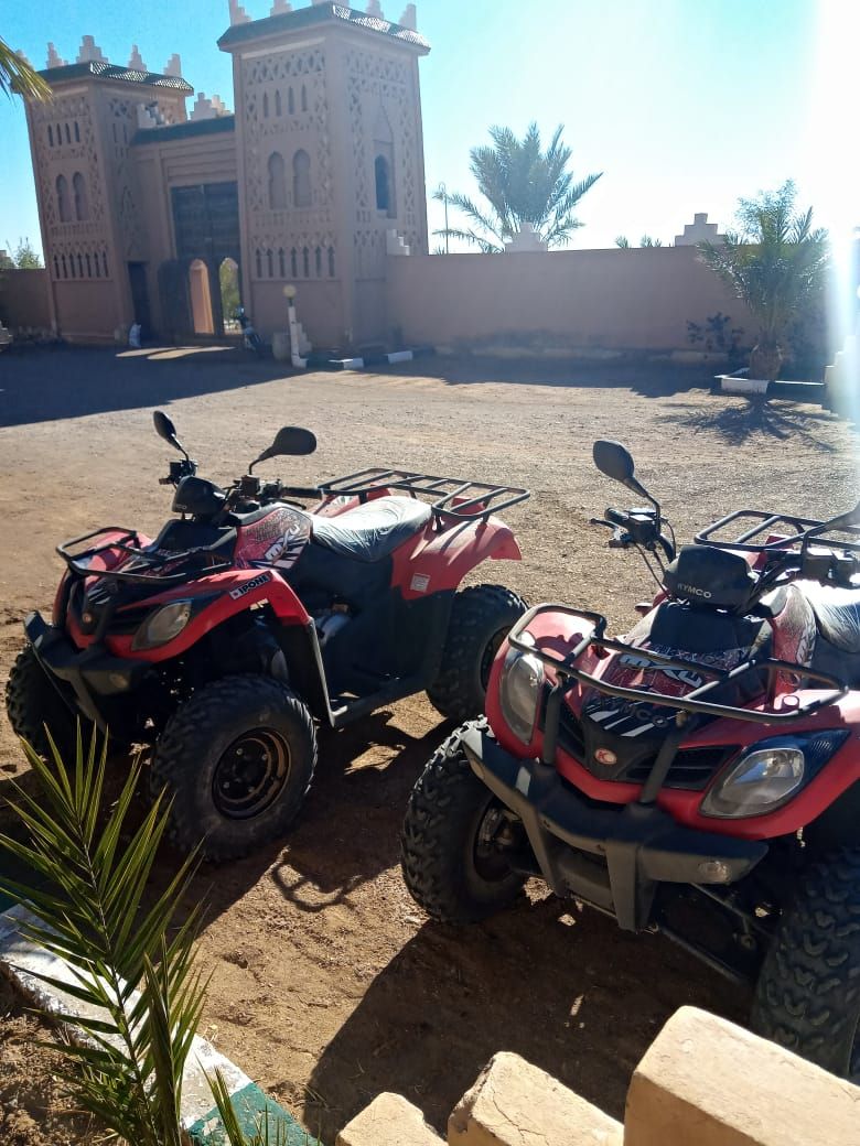Two red ATVs parked in a sandy area with a large building in the background.