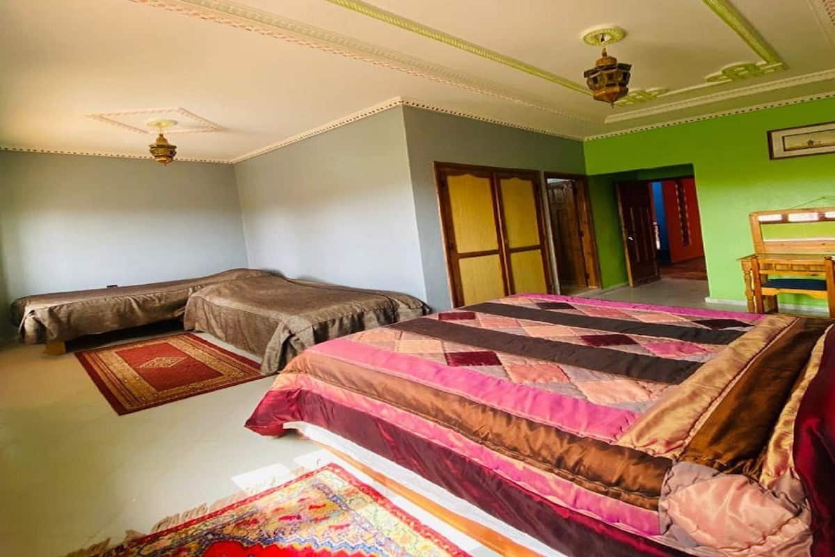 Une chambre avec un grand lit, deux petits lits, un ventilateur de plafond et un mur vert.