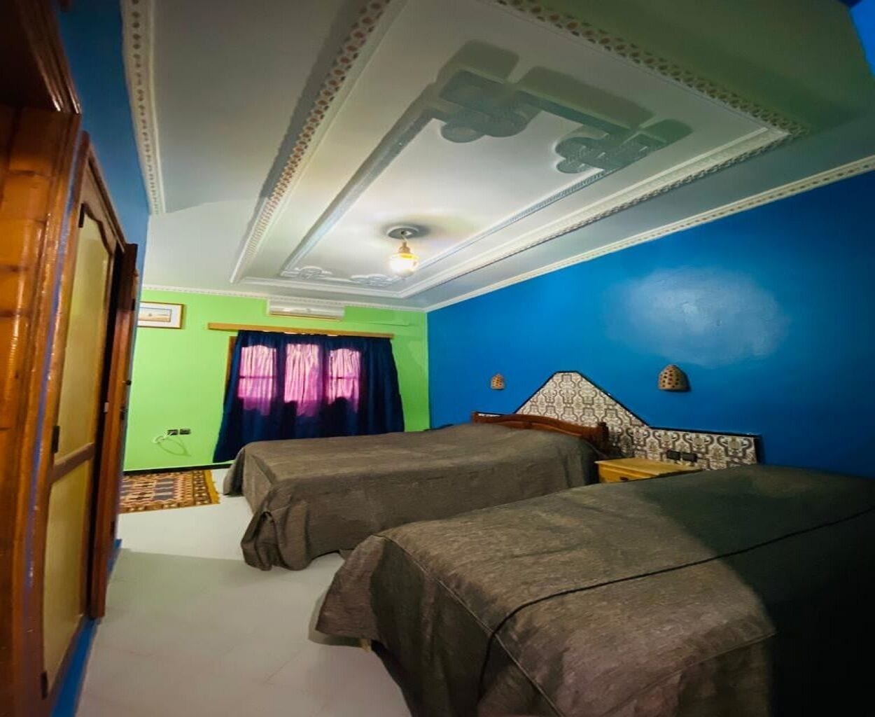 A room with two beds, a green wall, a blue accent wall, and a patterned ceiling.
