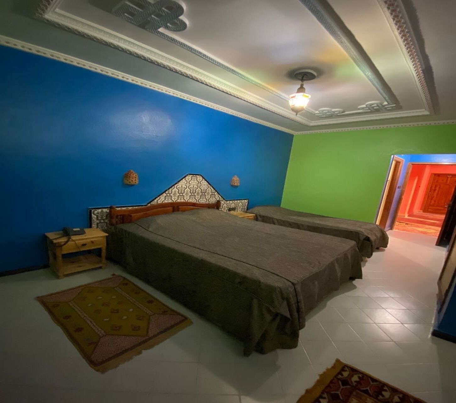 A bedroom with two beds, a nightstand, a patterned rug, and a ceiling light.