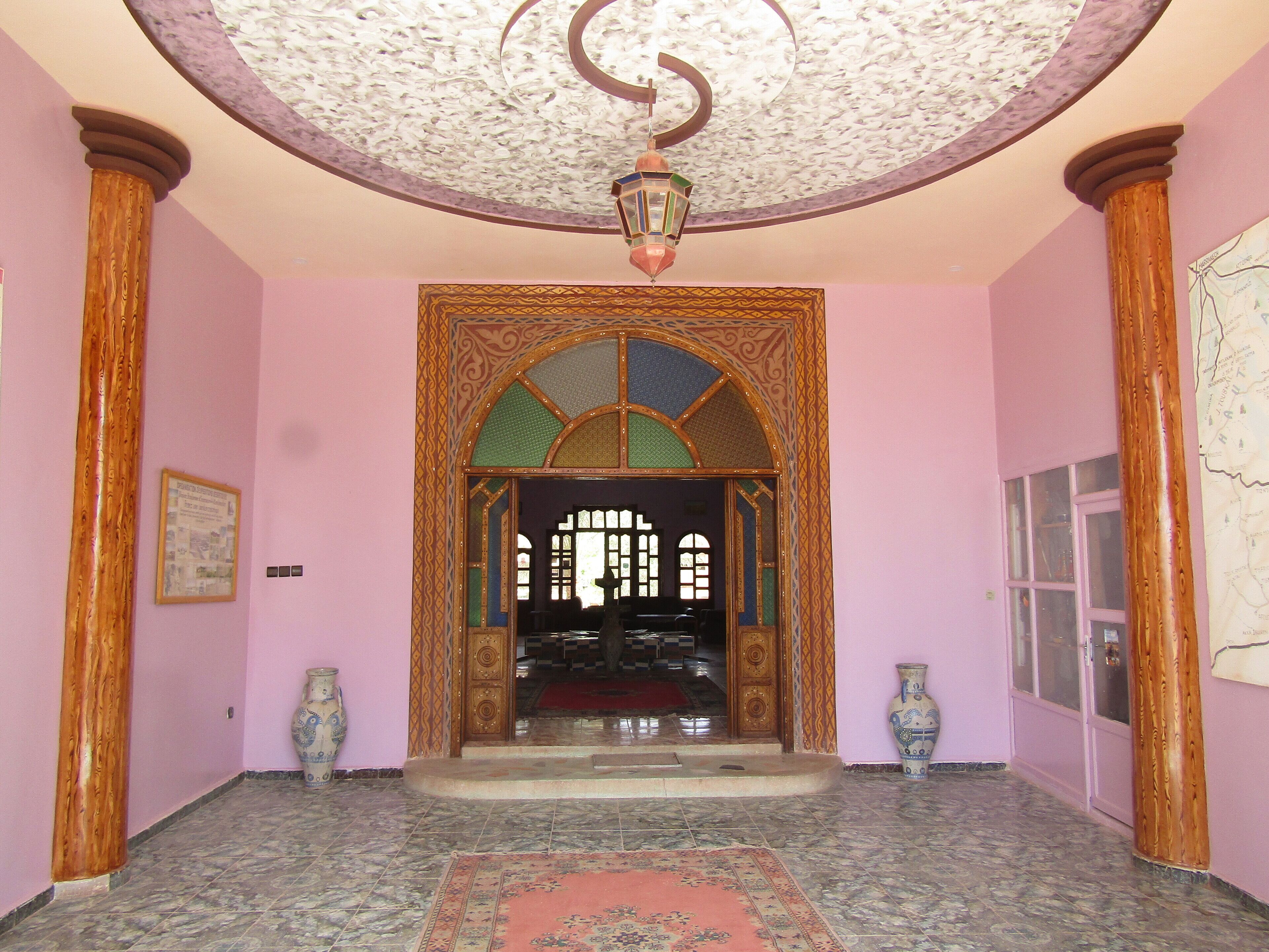 A hallway with a patterned archway, wooden columns, and a tiled floor.