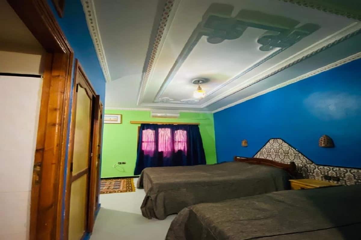 Une chambre avec deux lits, un mur orné de motifs, un plafond décoré et une porte située à gauche.