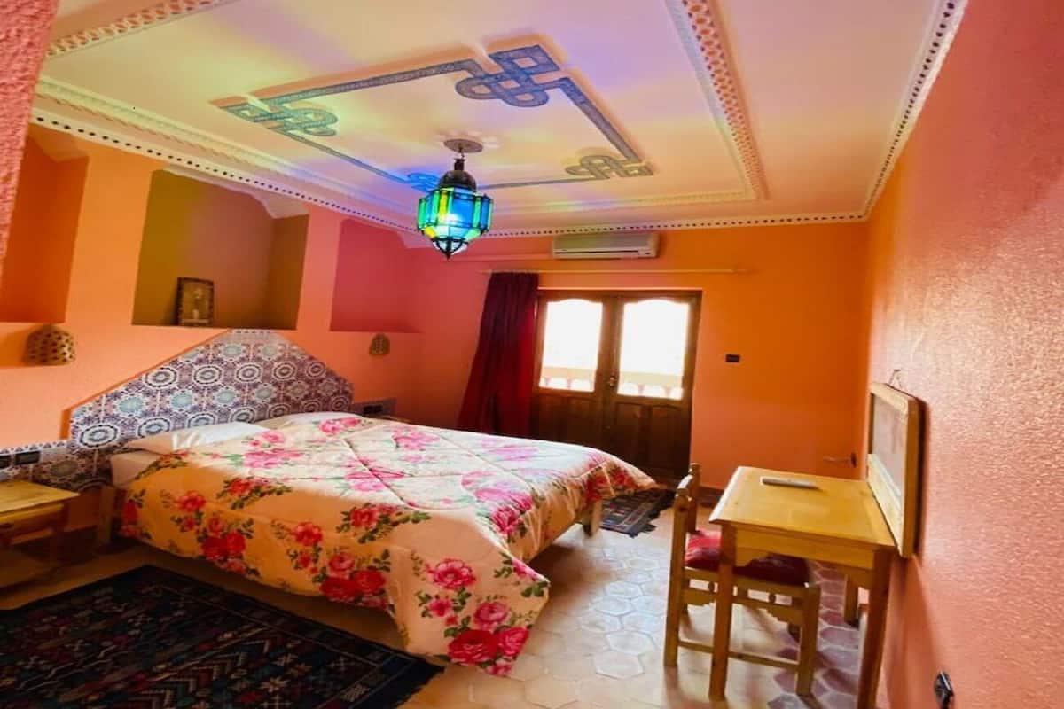 Une chambre à coucher comprenant un lit, un bureau, une chaise, un tapis à motifs et un plafond agrémenté d’un luminaire décoratif.