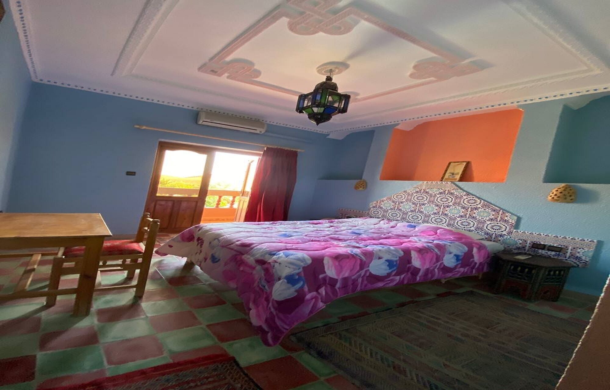 A bedroom with a bed, a desk, a chair, a window with curtains, and a ceiling fan.