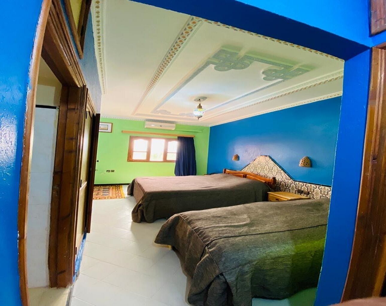 Una habitación con dos camas, una ventana con cortinas, un papel pintado y molduras decorativas en el techo.