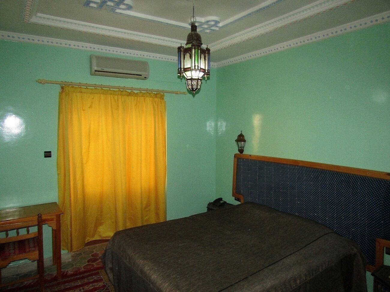 A bedroom with a bed, a wooden nightstand, a yellow curtain, a ceiling fan, and a hanging light fixture.