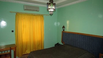 A bedroom with a bed, a wooden nightstand, a yellow curtain, a ceiling fan, and a hanging light fixture.