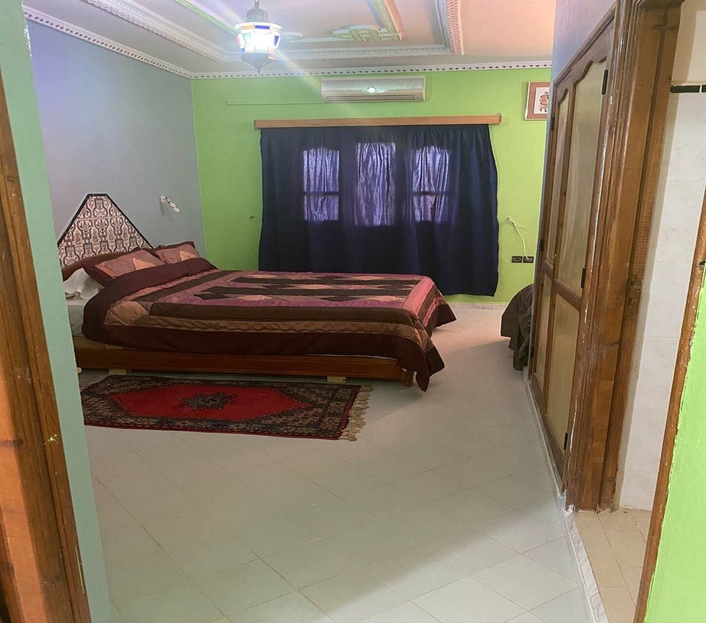 A bedroom with a bed, a red rug, and a window with dark curtains.