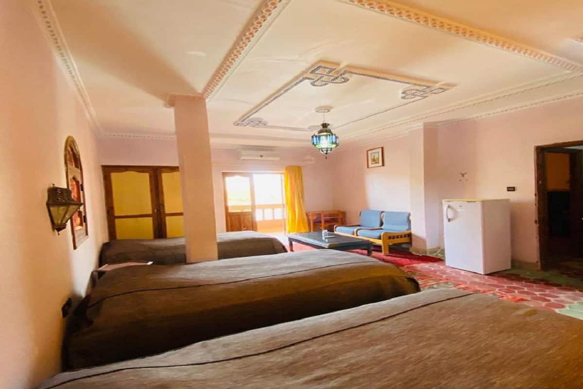 Une chambre avec deux lits, un bureau, une chaise, une petite table, un réfrigérateur et une fenêtre avec des rideaux.