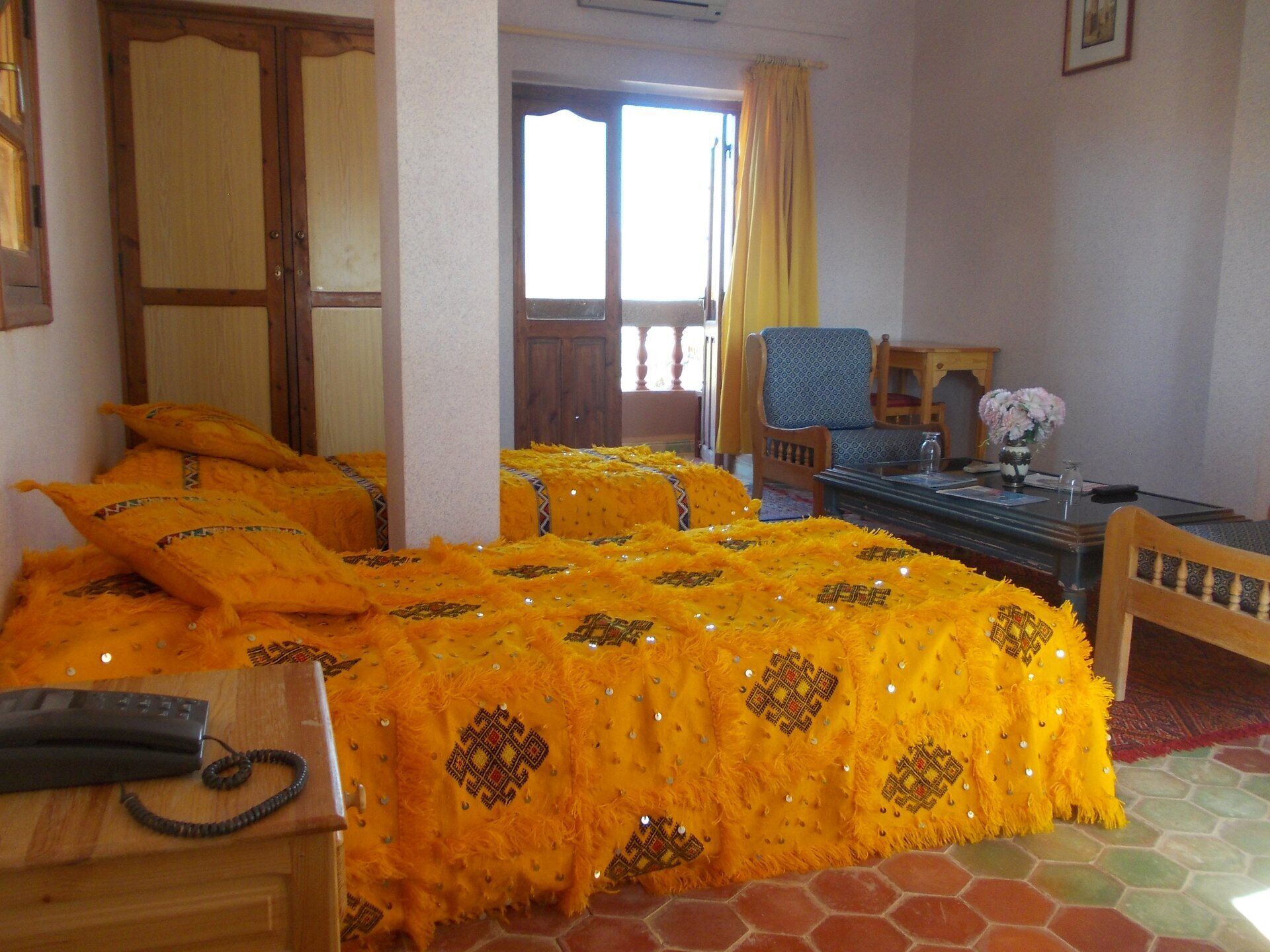 A room with two beds covered in bright yellow blankets, a wooden desk with a telephone, and a chair.