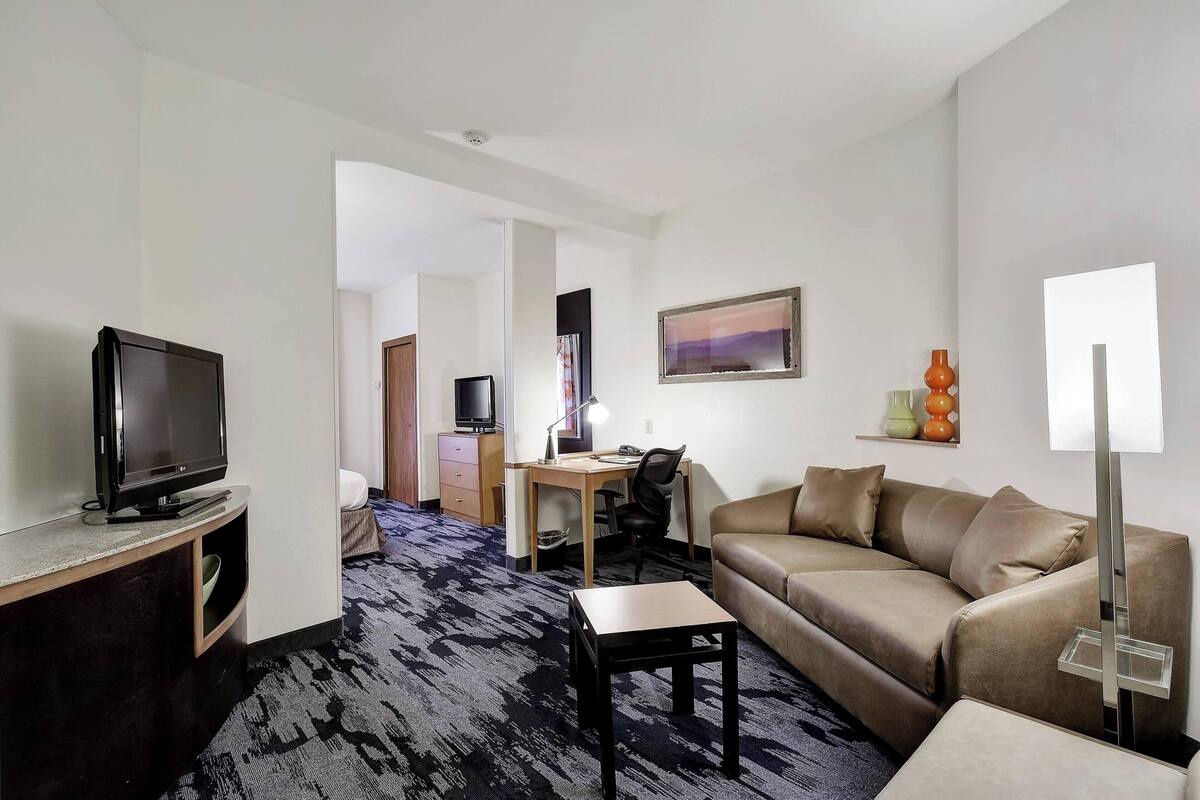 A hotel room with a TV, a desk, a computer, a sofa, and a lamp.