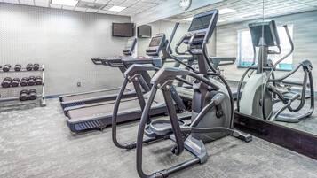 Un gimnasio con cintas de correr, elípticas y un estante con mancuernas.