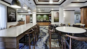 Um hall de hotel moderno com área de bar, espaços de estar e uma parede decorativa com texto motivacional.