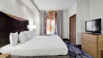 A hotel room with a large bed, a flat-screen TV, a wooden dresser, and a window with curtains.