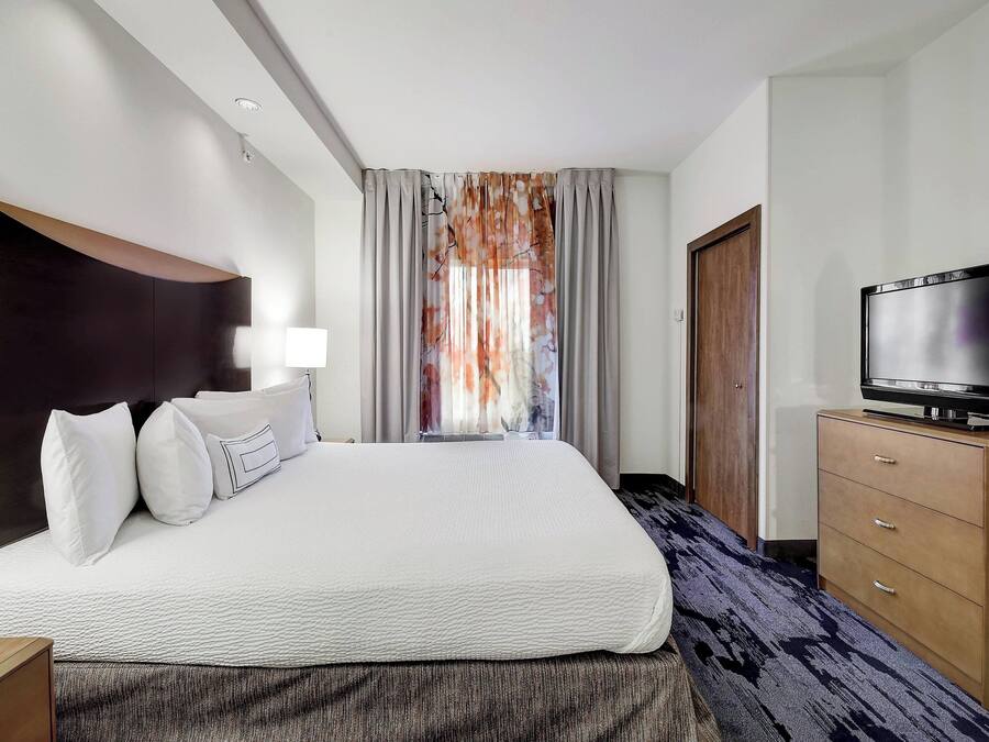 A hotel room with a large bed, a flat-screen TV, a wooden dresser, and a window with curtains.