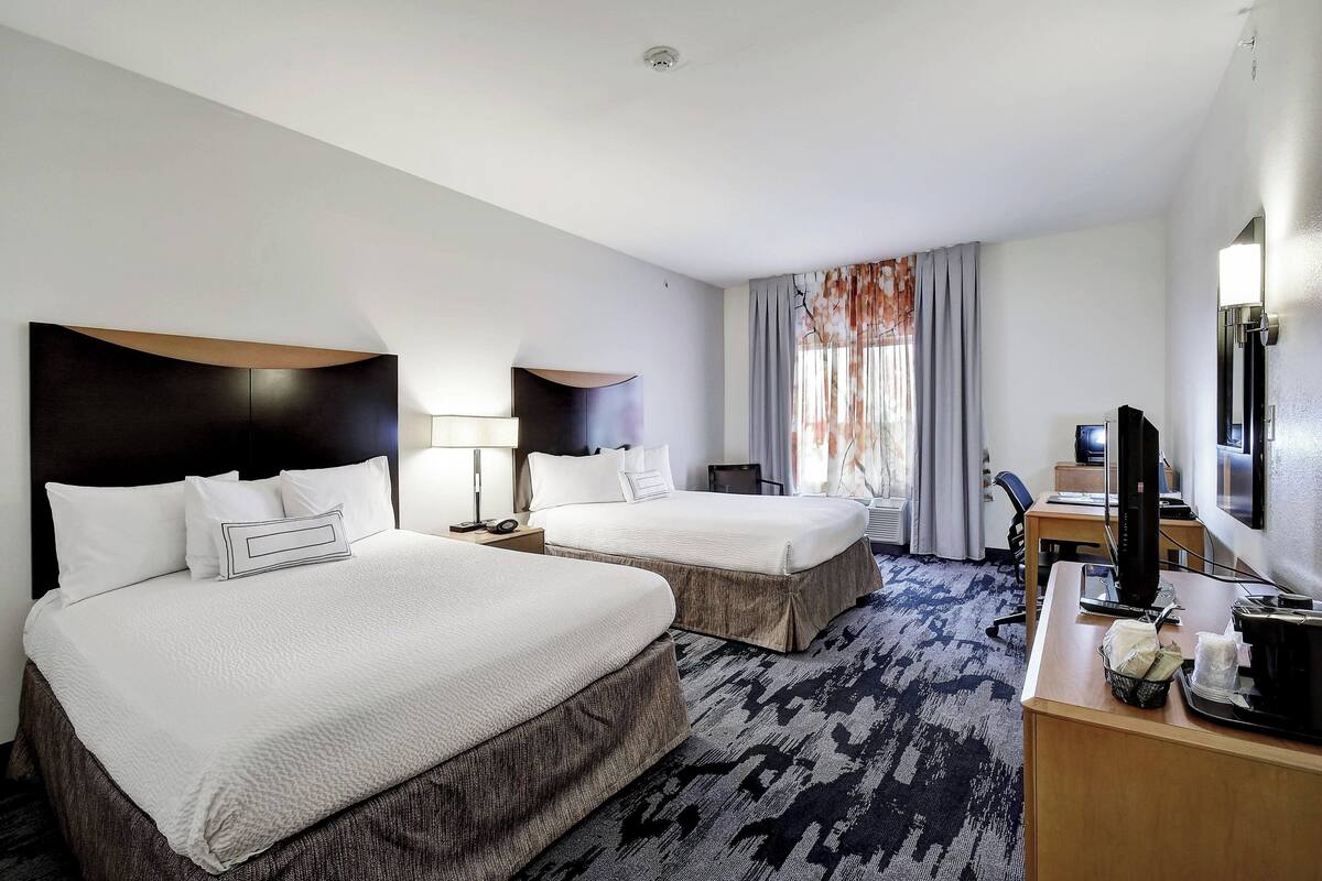 A hotel room with two beds, a desk with a computer, a TV, and a window with curtains.