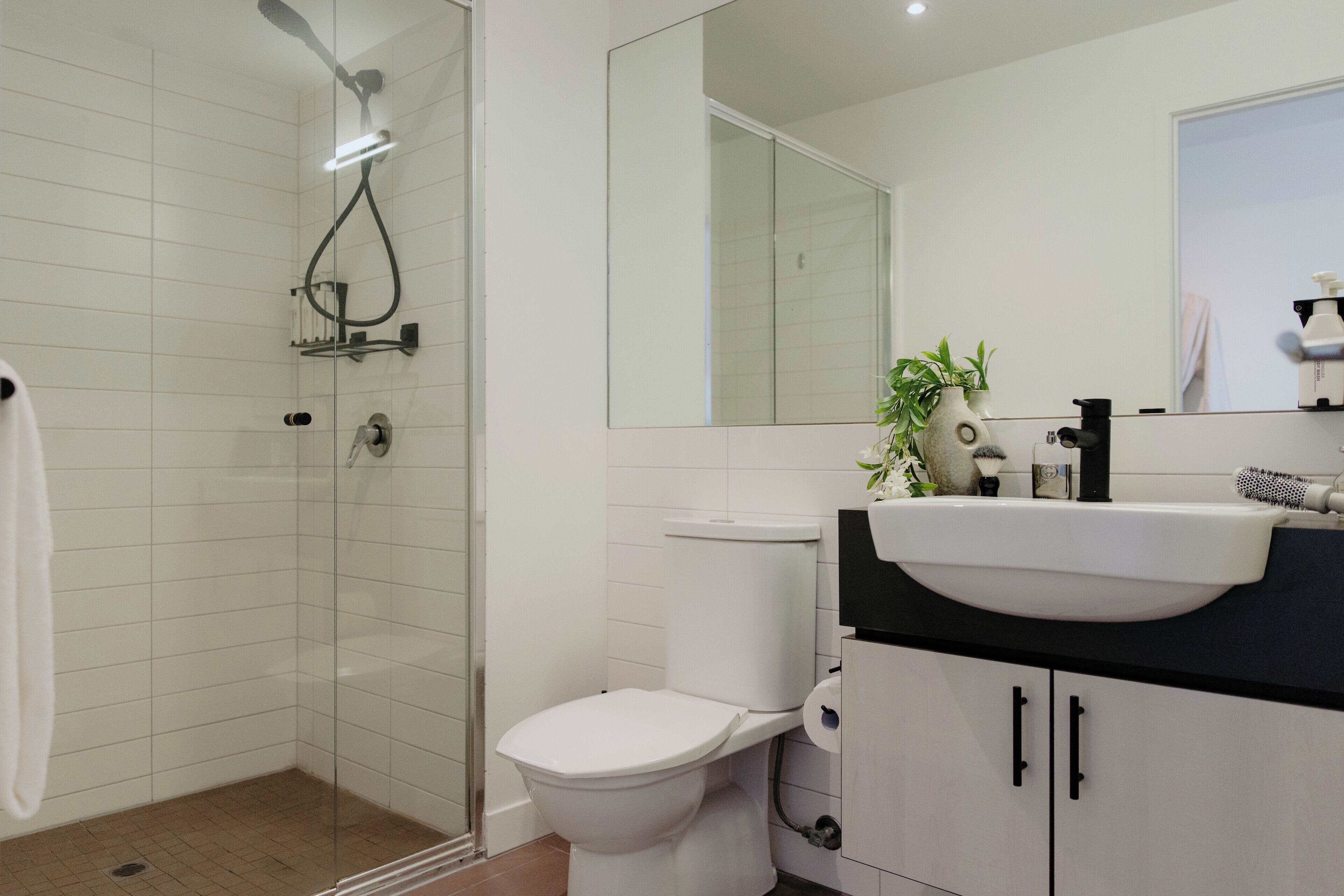 Een moderne badkamer met een glazen douchecabine, een wit toilet, een wastafel met een zwart aanrechtblad en een spiegel boven de wastafel.