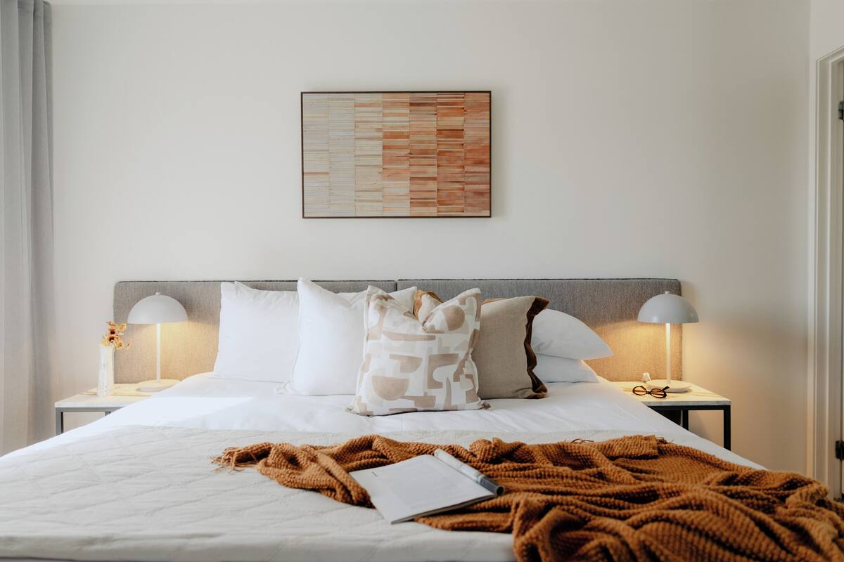 A neatly made bed with a patterned pillow, two bedside lamps, and a framed artwork on the wall.