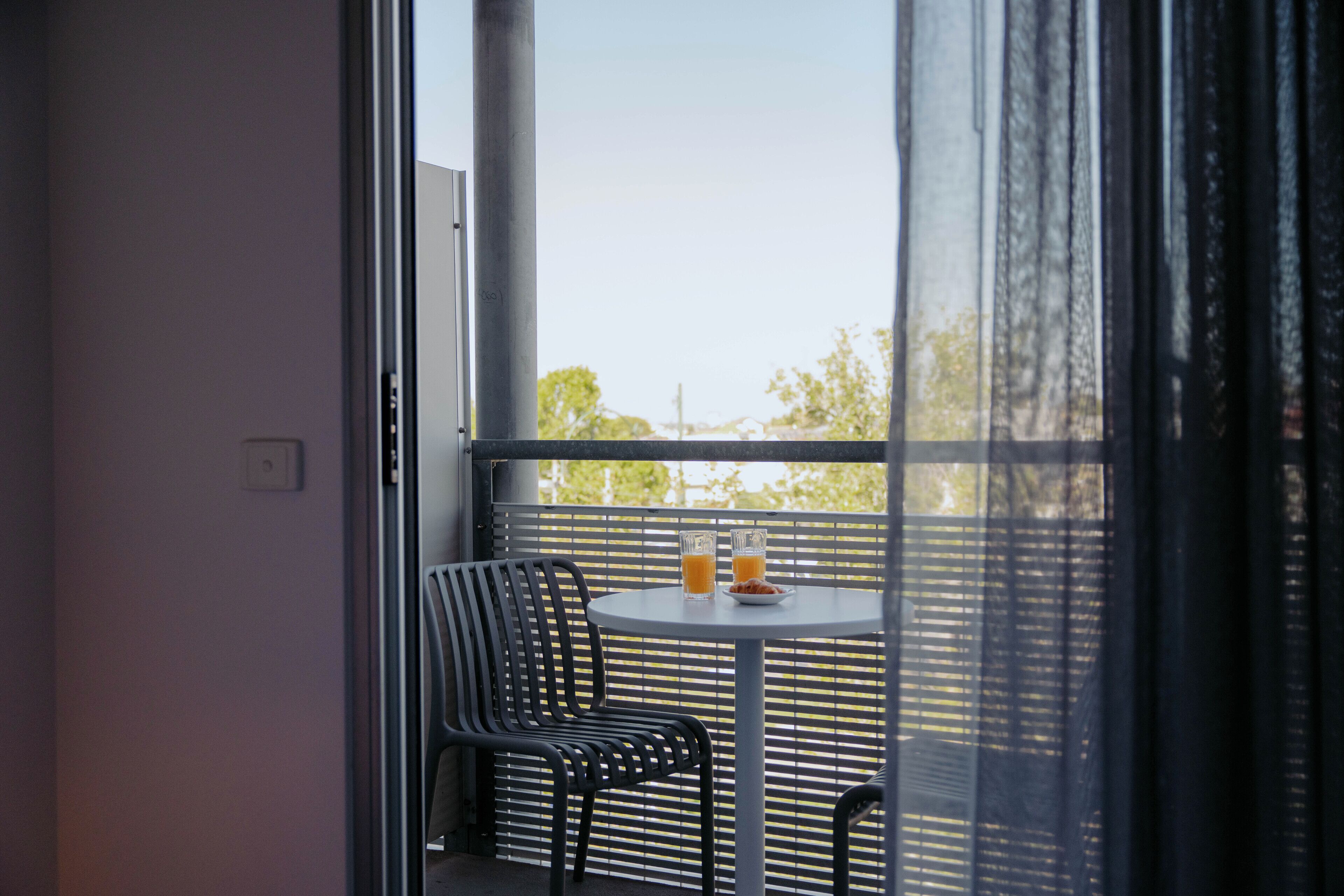 A balcony with a table, two chairs, and a window with blinds.
