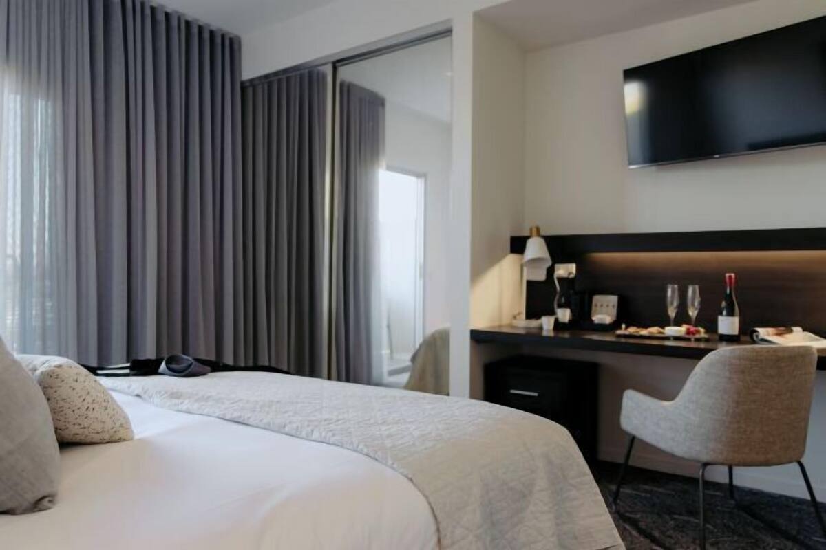 A hotel room with a bed, a desk with a lamp, a flat-screen TV, and a minibar.