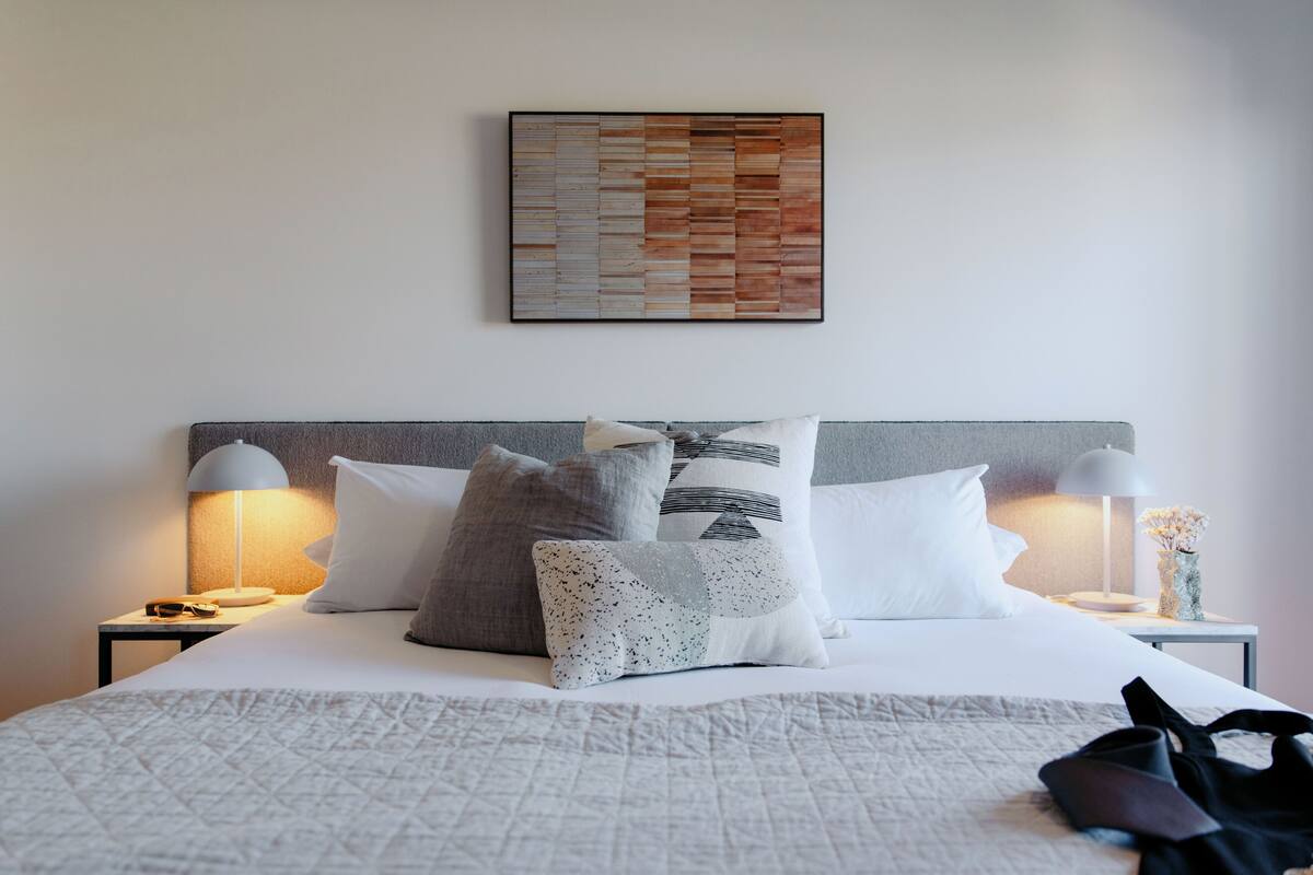 A neatly made bed with a quilt, pillows, and a pair of shoes on the bed.