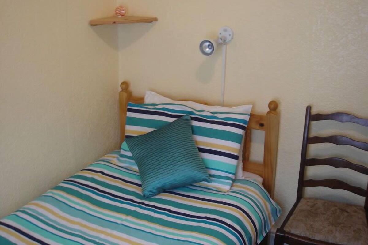 Una cama individual con una colcha a rayas, un almohábil de color turquesa y un cabecero de madera.