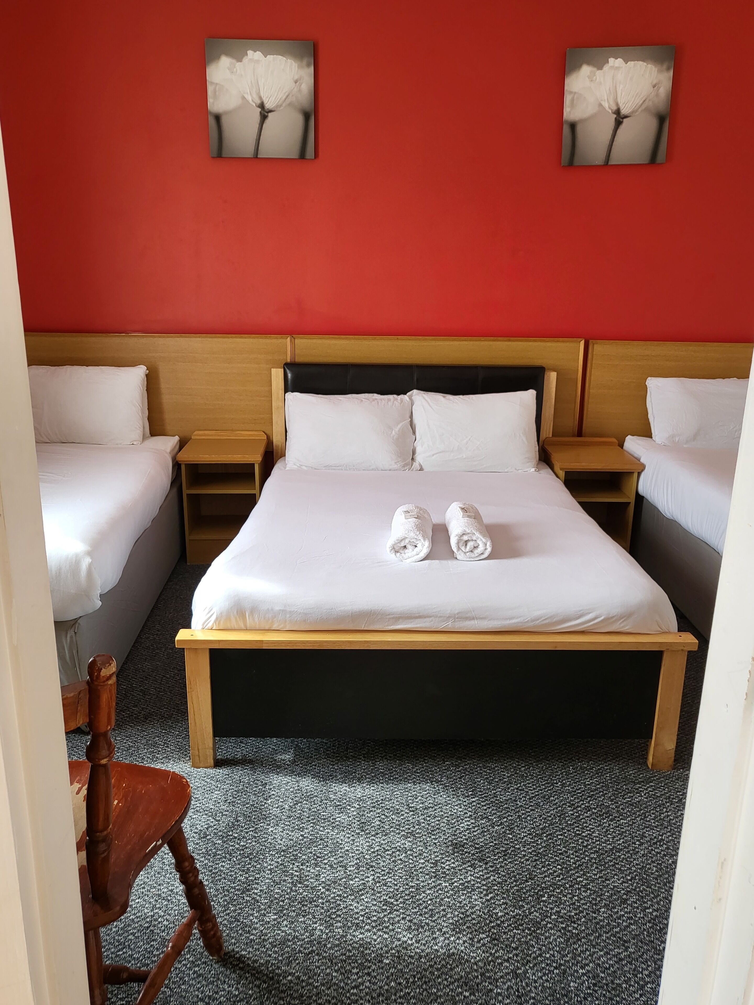 Habitación de hotel con una cama grande, dos mesitas de noche y una silla. Hay dos cuadros en la pared sobre la cama.