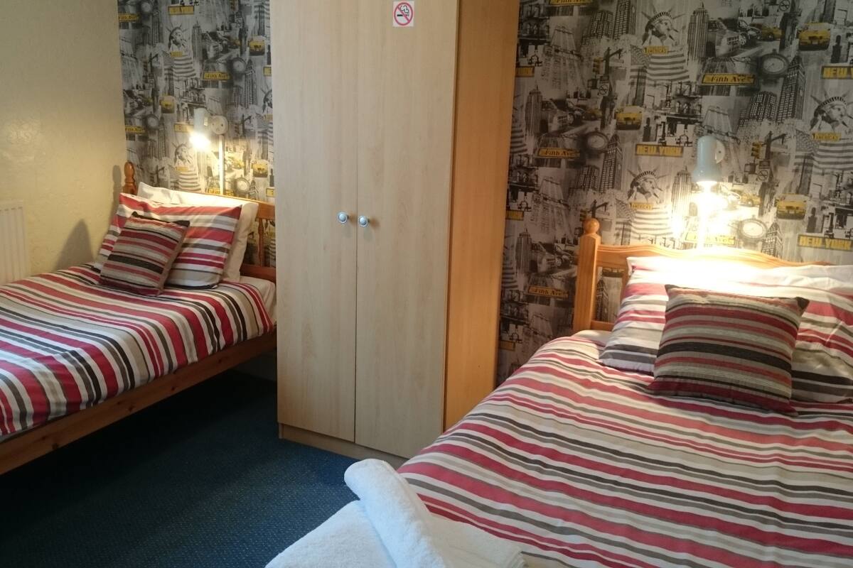 Una habitación con dos camas individuales, cada una con ropa de cama y almohadas a rayas, un armario de madera y un papel tapiz con vista urbana.