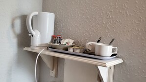 A small white shelf with a white mug, a coffee maker, and some packets on it.