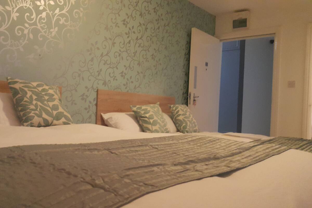 Un letto rifatto con cuscini decorati, una testiera in legno e carta da parati a motivi floreali.