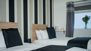 A hotel room with two beds, a wooden headboard, a bedside table with a lamp, and a window with curtains. - The Maple Hotel (Liverpool)