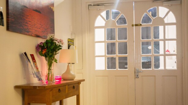 A wooden console table with a vase of flowers, a lamp, and a framed picture. - The Maple Hotel (Liverpool)