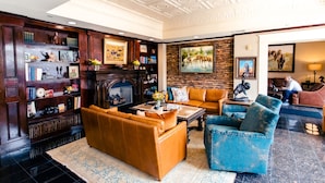 A spacious living room with a fireplace, leather sofas, a coffee table, and a bookshelf filled with books and decorative items. - The Grand Hotel (McKinney)